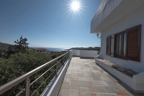 Un balcon doté d’une balustrade en métal, d’un sol carrelé et offrant une vue sur la mer et les bâtiments éloignés.