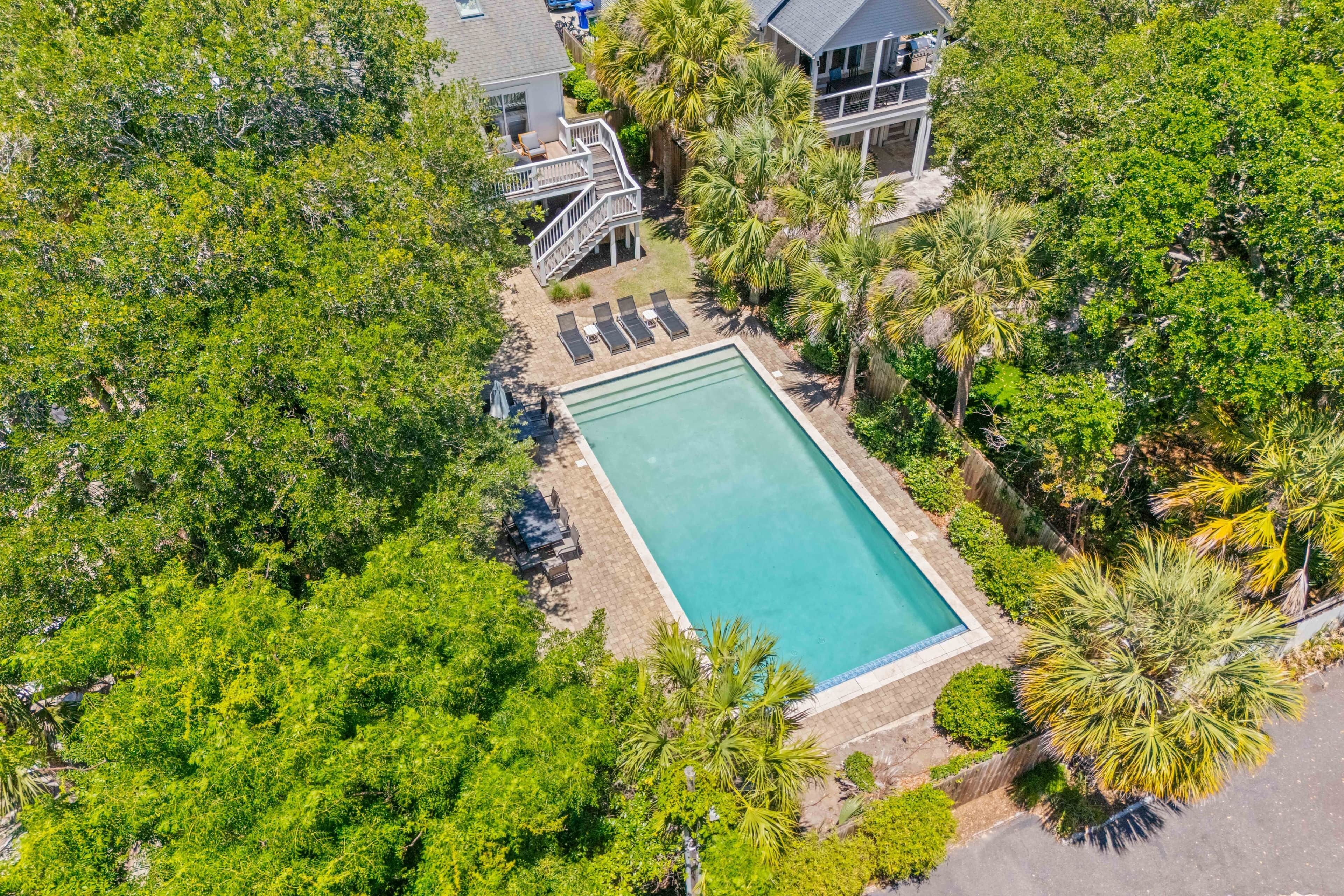 An aerial view of a property with a swimming pool surrounded by lush greenery and a multi-level building.