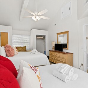 Habitación de hotel con dos camas, ventilador de techo, televisor, cómoda y espejo.
