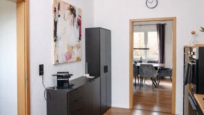 A modern room with a desk, a cabinet, a painting, a dining area with chairs, and a clock on the wall. - Vacation home in secluded location near Eifel National Park (Mechernich)