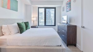 Una camera da letto con un letto grande, una cassettiera, una TV e una finestra vista città.