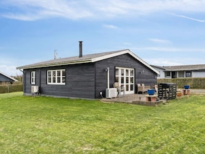 A single-story building with a dark exterior, a chimney, and a small patio area with outdoor furniture. - 4 Star Holiday Home in Roslev (Roslev)