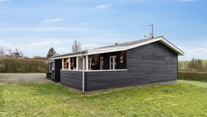 A small, dark wooden building with a sloped roof and a white porch. - 4 Star Holiday Home in Roslev (Roslev)