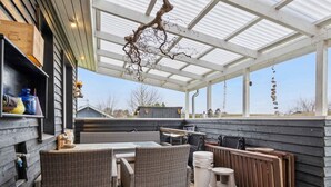 A covered patio with wicker furniture, a table, and a hanging branch. - 4 Star Holiday Home in Roslev (Roslev)