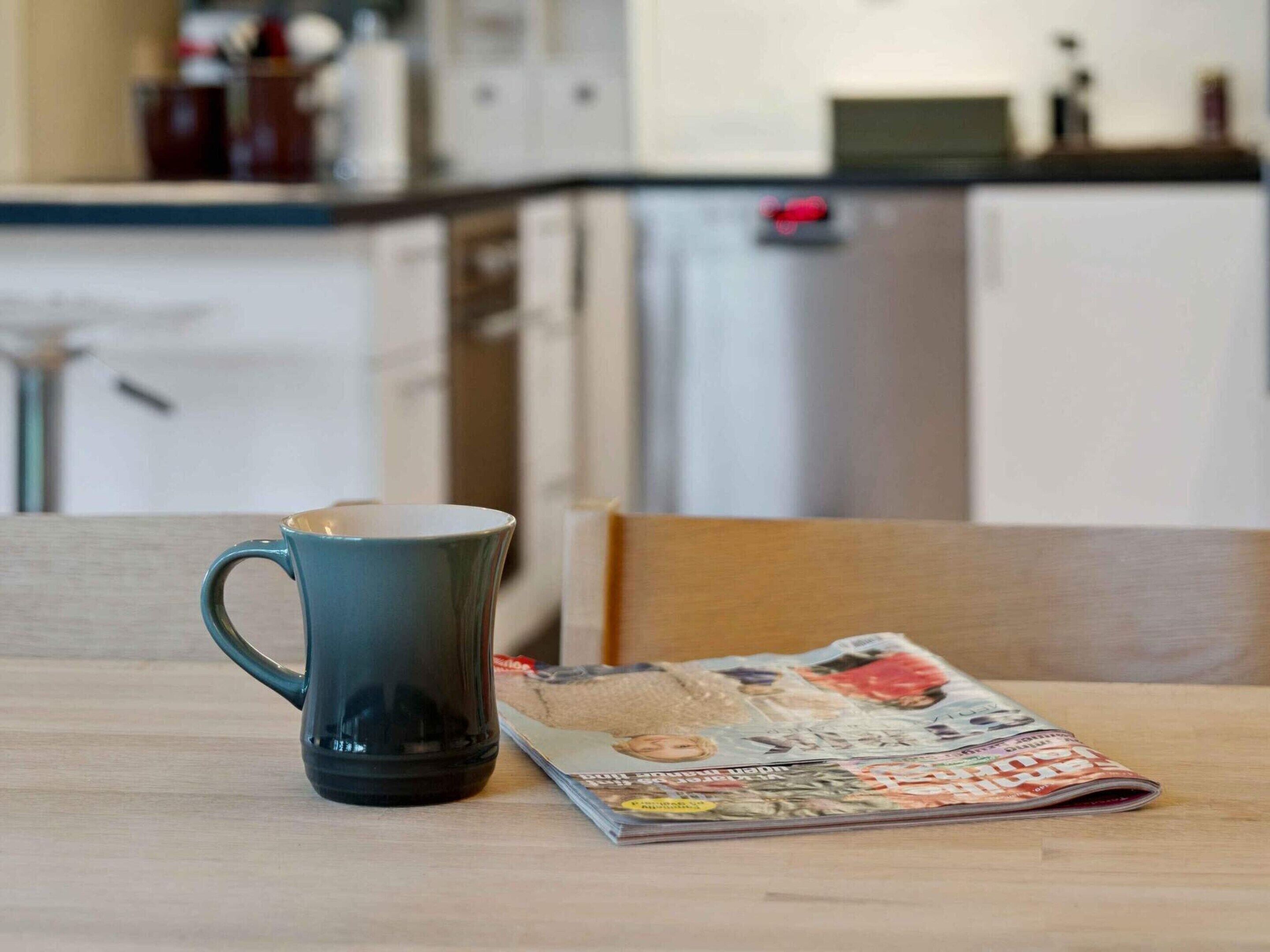 A kitchen area with a coffee mug and a magazine on the table.