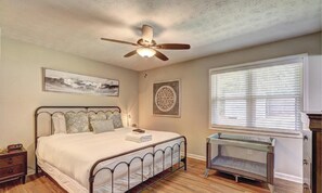 A bedroom with a bed, a ceiling fan, a window with blinds, a bedside table, and a wall-mounted artwork. - Chop House - King Bed, Smart TVs & Backyard Fun! (Douglasville)