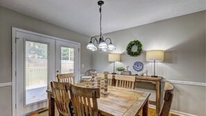 Un espace repas comprenant une table et des chaises en bois, un lustre et deux lampes fixées au mur.