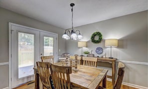 A dining area with a wooden table and chairs, a chandelier, and two wall-mounted lamps. - Chop House - King Bed, Smart TVs & Backyard Fun! (Douglasville)