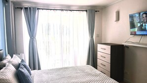 Ein Schlafzimmer mit einem Bett, einem Wandfernseher, einem Deckenventilator und einem Fenster mit Vorhängen.