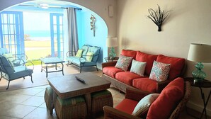 Ein Zimmer mit einem roten Sofa, Korbsesseln, einem Holztisch und einem Deckenventilator.