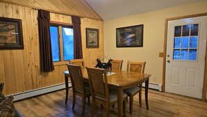 Un comedor con una mesa y sillas de madera, una puerta con ventanal y cuadros en las paredes.