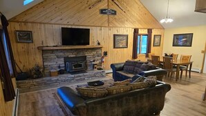 Una sala de estar acogedora con chimenea de piedra, televisor montado en la pared y comedor con muebles de madera.