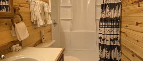 A wooden cabin bathroom with a bathtub, toilet, sink, and a mirror.