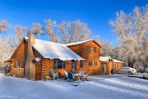 Une cabane en rondins avec une cheminée, un abri pour voiture et un toit recouvert de neige.