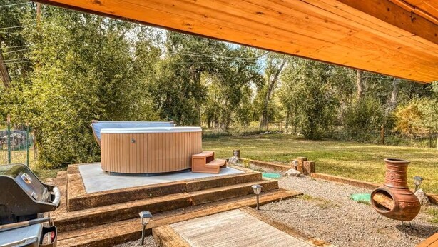 Un jacuzzi en una plataforma de madera con escalones, una parrilla y un entorno rústico al aire libre.