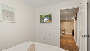 A bedroom with a bed, a TV mounted on the wall, and a door leading to a dining area. - Rooftop Deck Chinatown Getaway w/Shared Gamroom (Philadelphia)