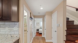 A hallway with a kitchen area, wooden flooring, and a staircase. - Rooftop Deck Chinatown Getaway w/Shared Gamroom (Philadelphia)