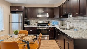 A modern kitchen with dark wood cabinets, stainless steel appliances, a granite countertop, and a dining area with a glass table and chairs. - Rooftop Deck Chinatown Getaway w/Shared Gamroom (Philadelphia)