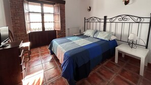 A bedroom with a bed, a desk, a window, and a brick wall.