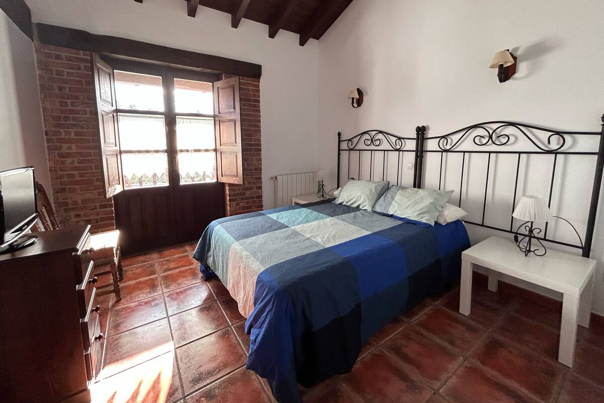 Ein Schlafzimmer mit Bett, Schreibtisch, Fenster und Backsteinwand.