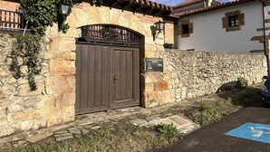 A stone wall with a metal gate, a paved area with a blue wheelchair symbol, and a clear sky.