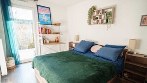Un dormitorio con una cama, una estantería, un estante en la pared y una ventana con cortinas.