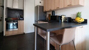 Una cocina moderna con armarios de madera, encimera negra, refrigerador de acero inoxidable, microondas, tostadora y frutero con una piña.