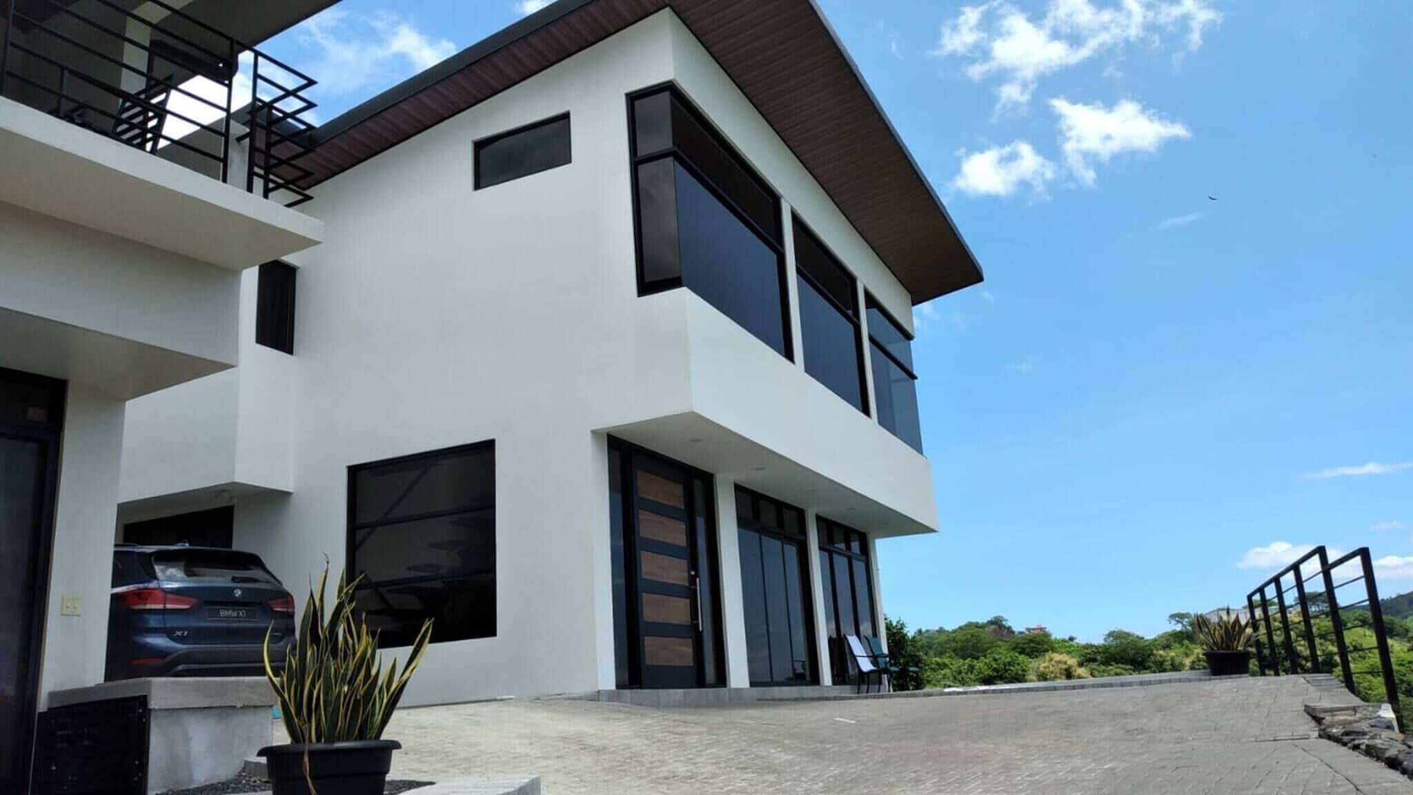 A modern two-story house with a car parked in the driveway and a potted plant in the foreground.