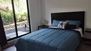 Ein Schlafzimmer mit einem großen Bett, einem Nachttisch, einem Fenster mit Blick auf Grünflächen und einer Steinsäule draußen.
