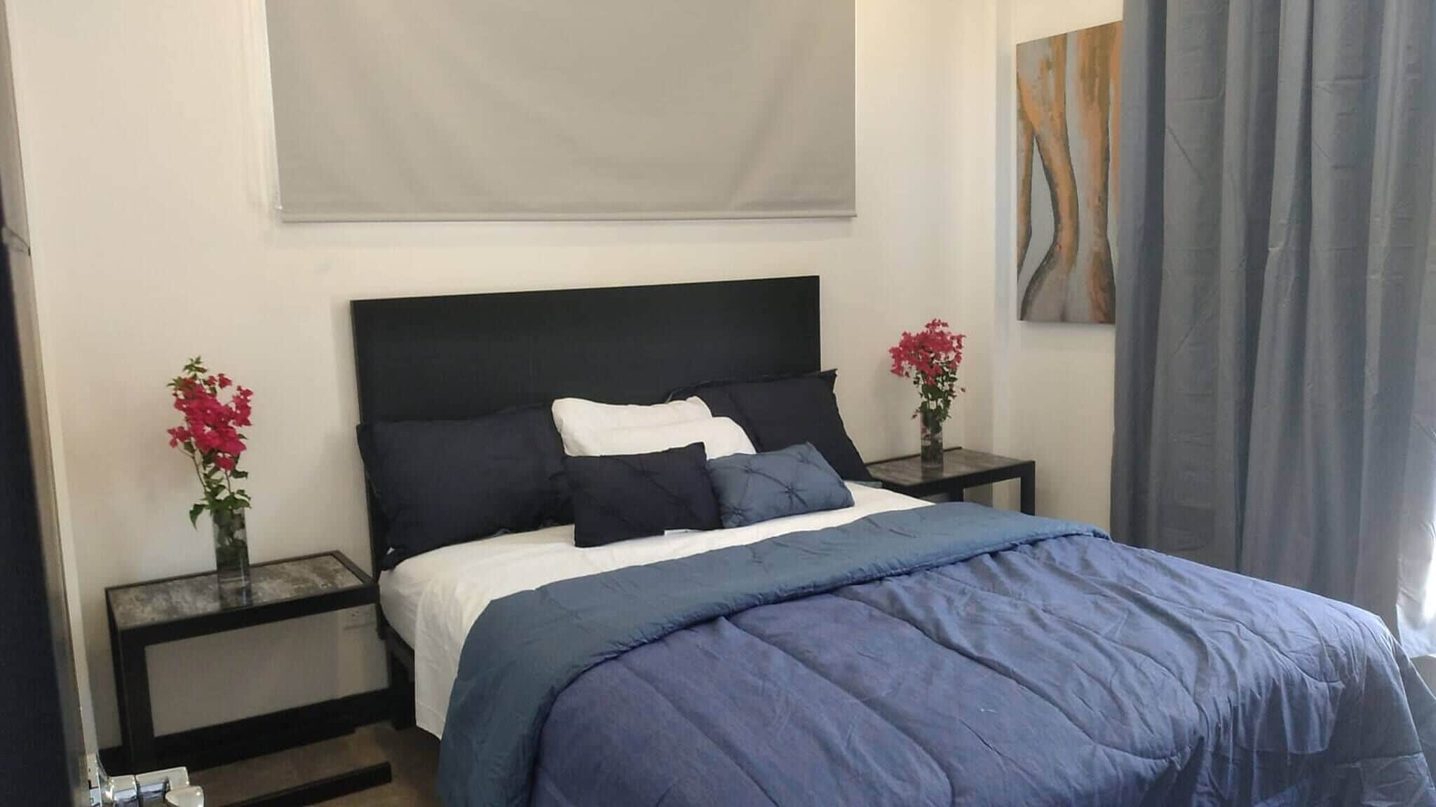 A hotel room with a bed, two nightstands, a window with curtains, and a painting on the wall.