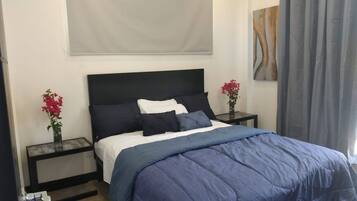 A hotel room with a bed, two nightstands, a window with curtains, and a painting on the wall.