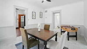 Een eetkamer met een houten tafel, stoelen, een plafondventilator en een tafelvoetbaltafel.