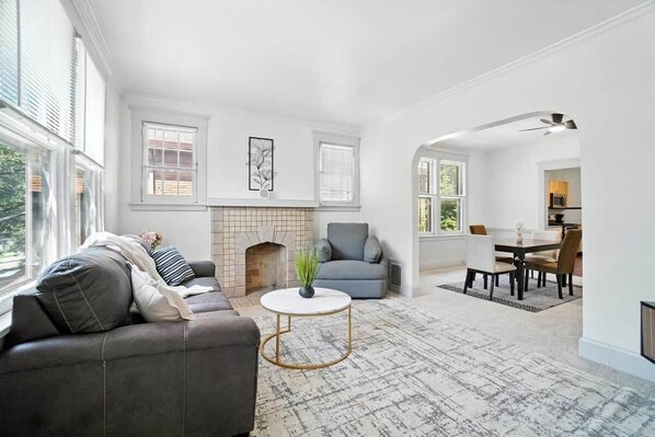 A living room with a fireplace, a sofa, a coffee table, and a dining area with chairs. - 3BR, Quiet Street, 10 Min DTW (Cincinnati)