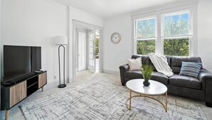 Een woonkamer met een televisie, bank, salontafel en een klok aan de muur.