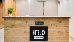 A reception desk with a wooden finish, a reception sign, an air conditioning unit, and a wall-mounted fan. - Deluxe OXY Royal Residency (Ranchi)