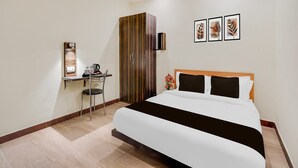 A hotel room with a bed, a desk with a chair, a wardrobe, and three framed pictures on the wall. - Deluxe OXY Royal Residency (Ranchi)