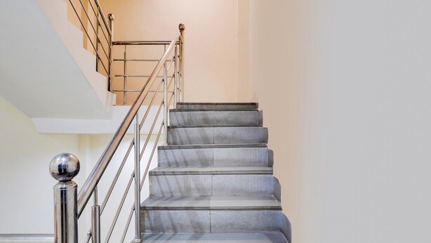 A staircase with metal railings and a ball finial, leading to a higher floor. - Deluxe OXY Royal Residency (Ranchi)