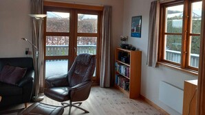 A room with a leather chair, a bookshelf, and large windows with a view of trees and a balcony. - 4 Star Holiday Home in Sjolund (Sjølund)
