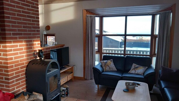 A living room with a fireplace, a sofa, a TV, and a view through large windows. - 4 Star Holiday Home in Sjolund (Sjølund)