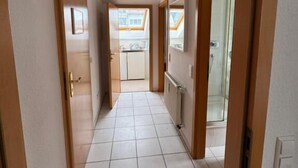 A hallway with tiled flooring, wooden doors, and a view into a kitchen area. - Haus Mechthild (Sindelfingen)