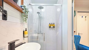 Un bagno con doccia vetrata, lavandino bianco e una sedia blu.