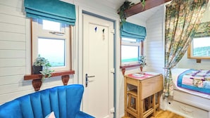 Una stanza con una sedia blu, un tavolo di legno e un letto con tende a fiori.