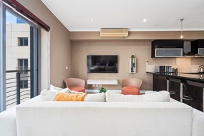 A modern living room with a sofa, two armchairs, a flat-screen TV, and a kitchen area with a bar. - Icon 606 (Cape Town)