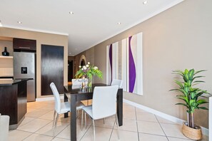 A modern kitchen with a built-in refrigerator, a dining area with a table and chairs, and a decorative wall with abstract art. - Icon 606 (Cape Town)