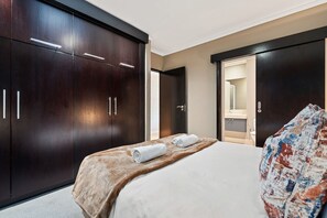 A hotel room with a bed, a large wardrobe, a mirror, and a bathroom visible through an open door. - Icon 606 (Cape Town)