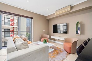Un salon moderne comprenant un canapé, des fauteuils, une table basse, un téléviseur et une bibliothèque.