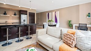 Una cocina moderna con taburetes de bar, un comedor con mesa y sillas, y una sala de estar con sofá y cojines.