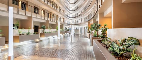 Un atrium à plusieurs niveaux, doté d’un sol carrelé, de rampes et de jardinières agrémentées de plantes vertes.