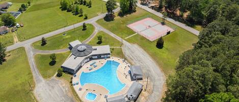 An aerial view of a residential area with a swimming pool, a tennis court, and a large building with a circular roof.