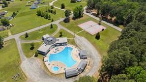 Vista aérea de una zona residencial con piscina, cancha de tenis y un edificio grande con techo circular.
